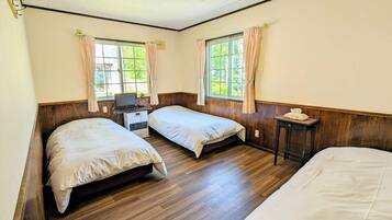 A room with two beds, a desk with a laptop, and a window with curtains.
