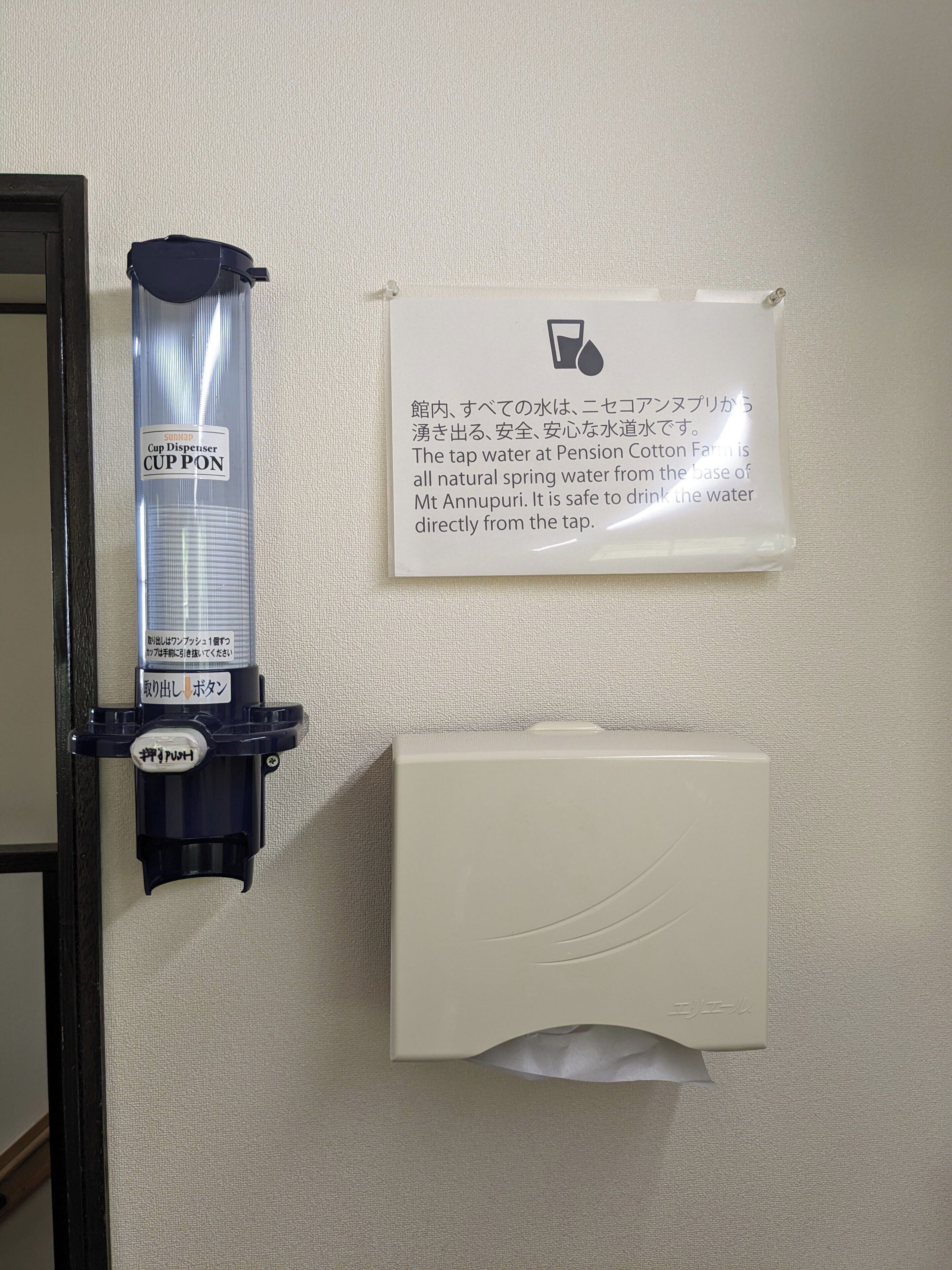 Een bekerdispenser aan de muur en een bord met instructies in zowel Japans als Engels.