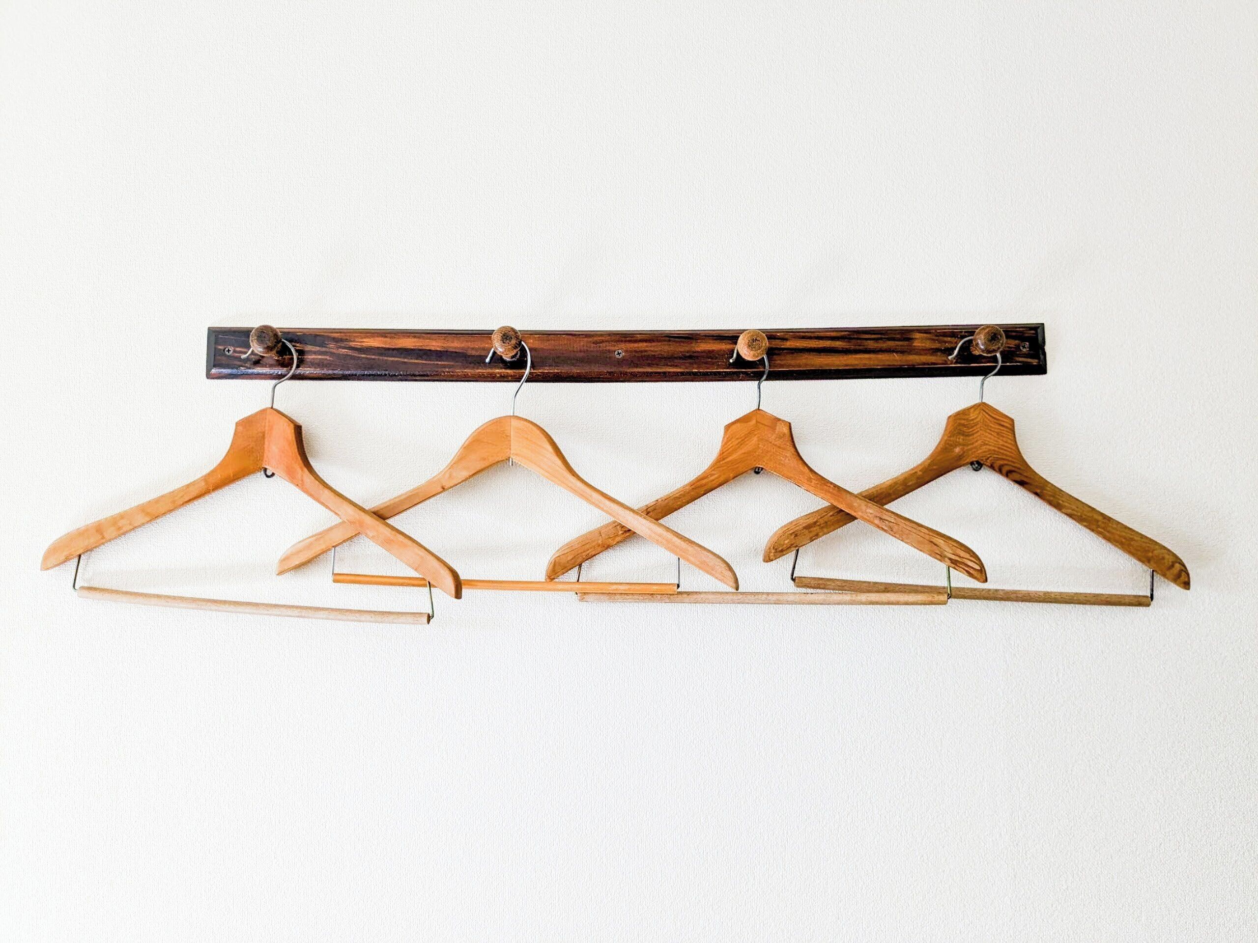 Four wooden hangers on a wooden rack against a white wall.
