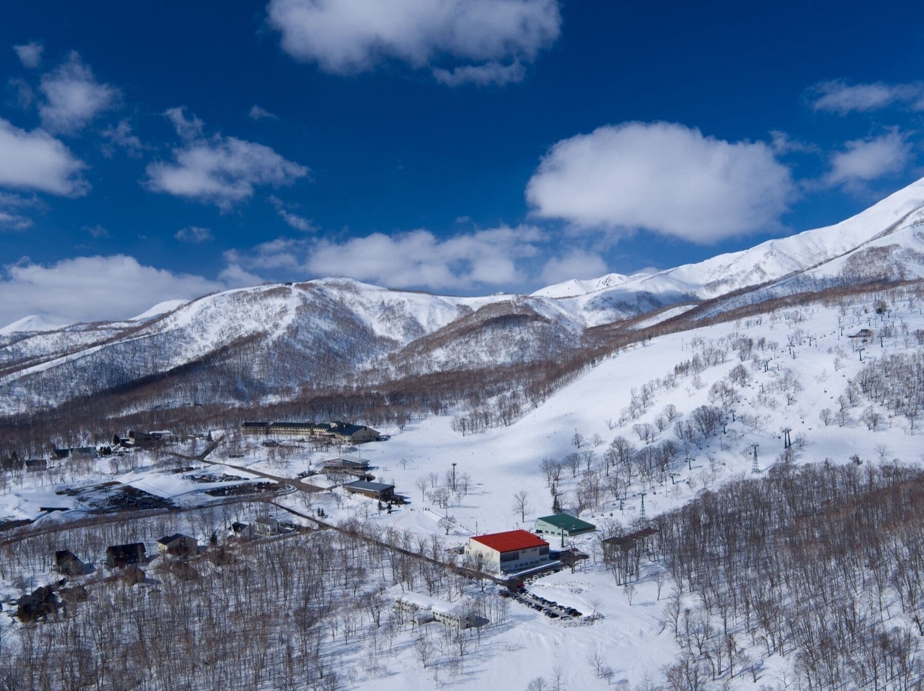 A snow-covered mountainous area with a ski resort, including buildings and ski lifts.