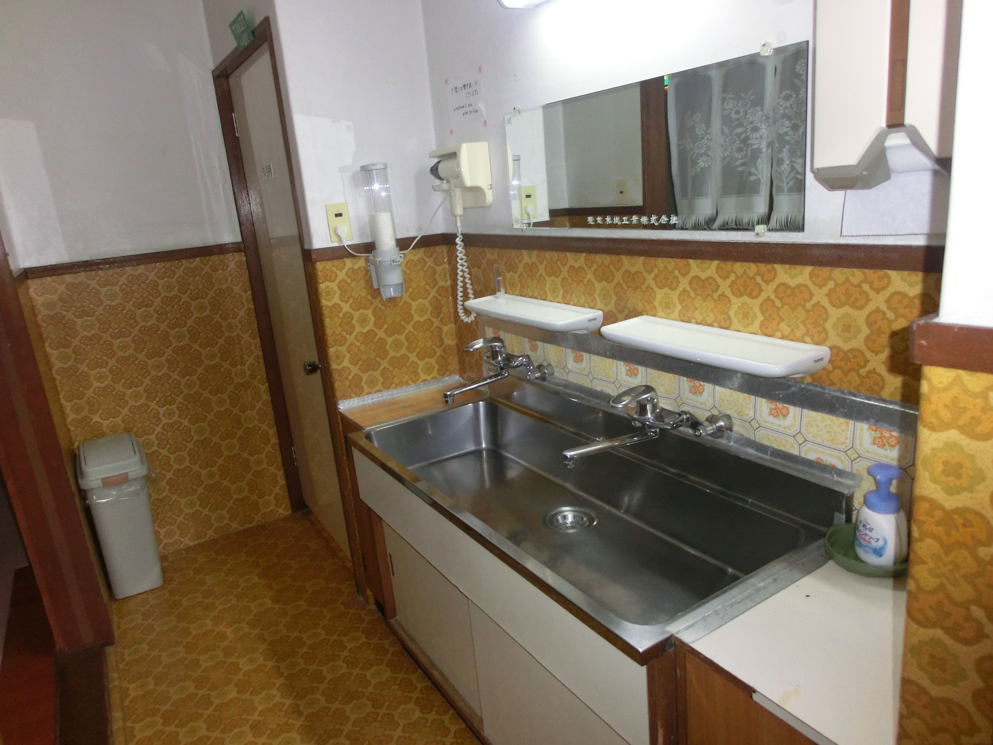 A compact kitchen with a stainless steel sink, a mirror above it, and a patterned backsplash.