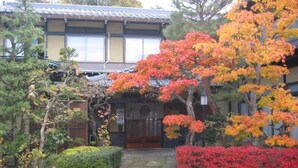 Een traditioneel Japans gebouw met een houten entree en een kleine tuin met herfstkleurige bomen.