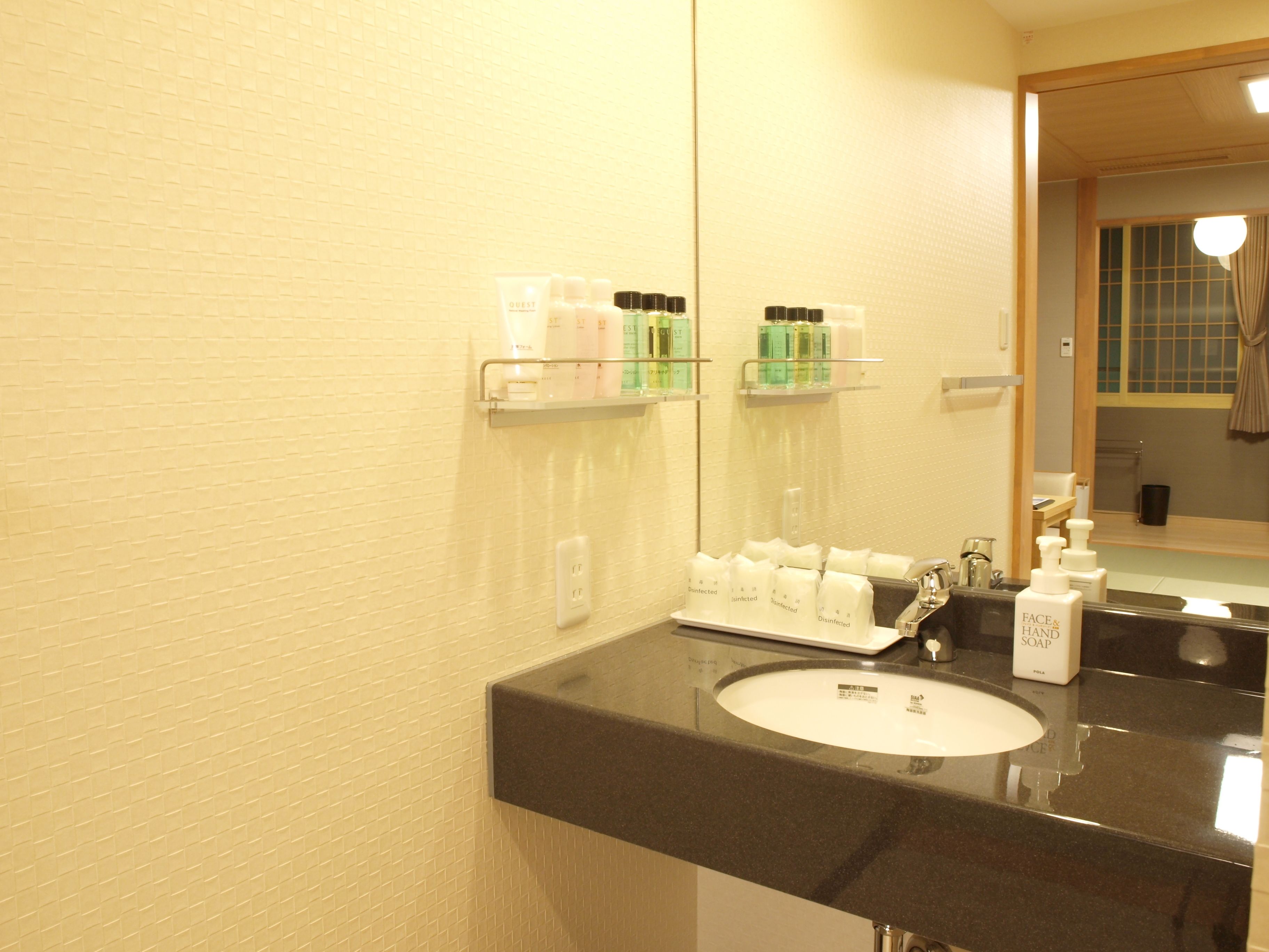Un bagno con un piano lavabo nero, lavandino bianco e mensole con articoli da toilette.
