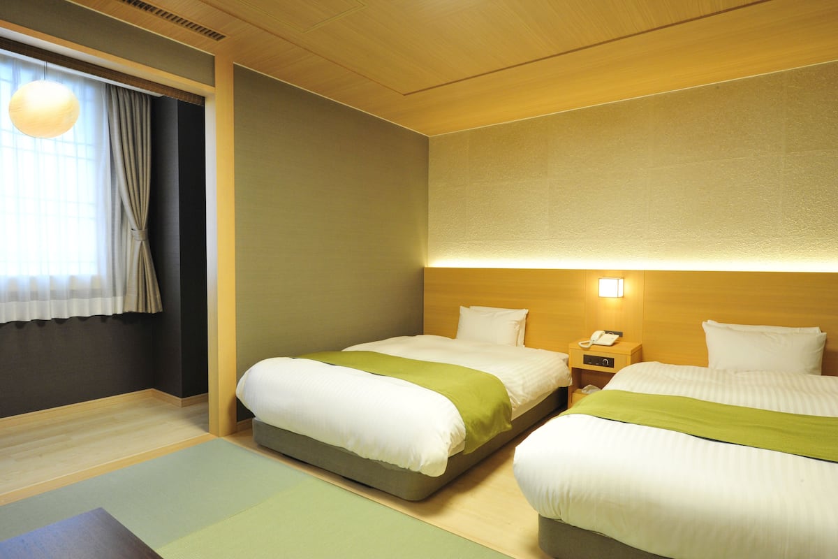 A hotel room with two beds, a bedside table with a phone, and a window with curtains.