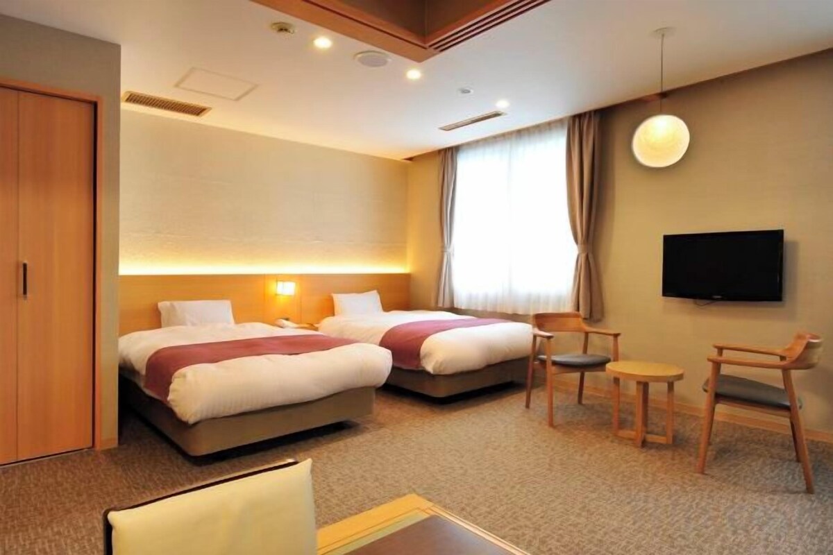 A hotel room with two beds, a TV, a desk, and a chair.