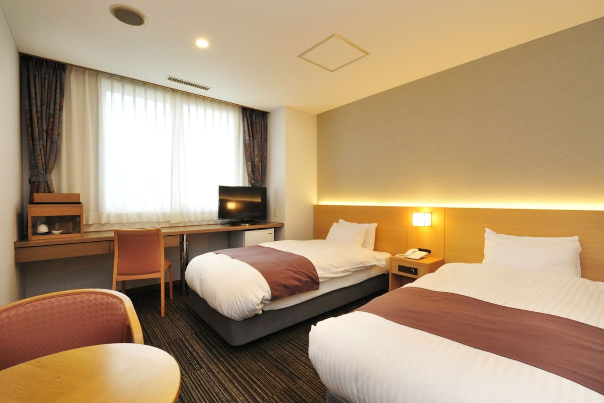 A hotel room with two beds, a desk, a chair, a television, and a nightstand with a phone.
