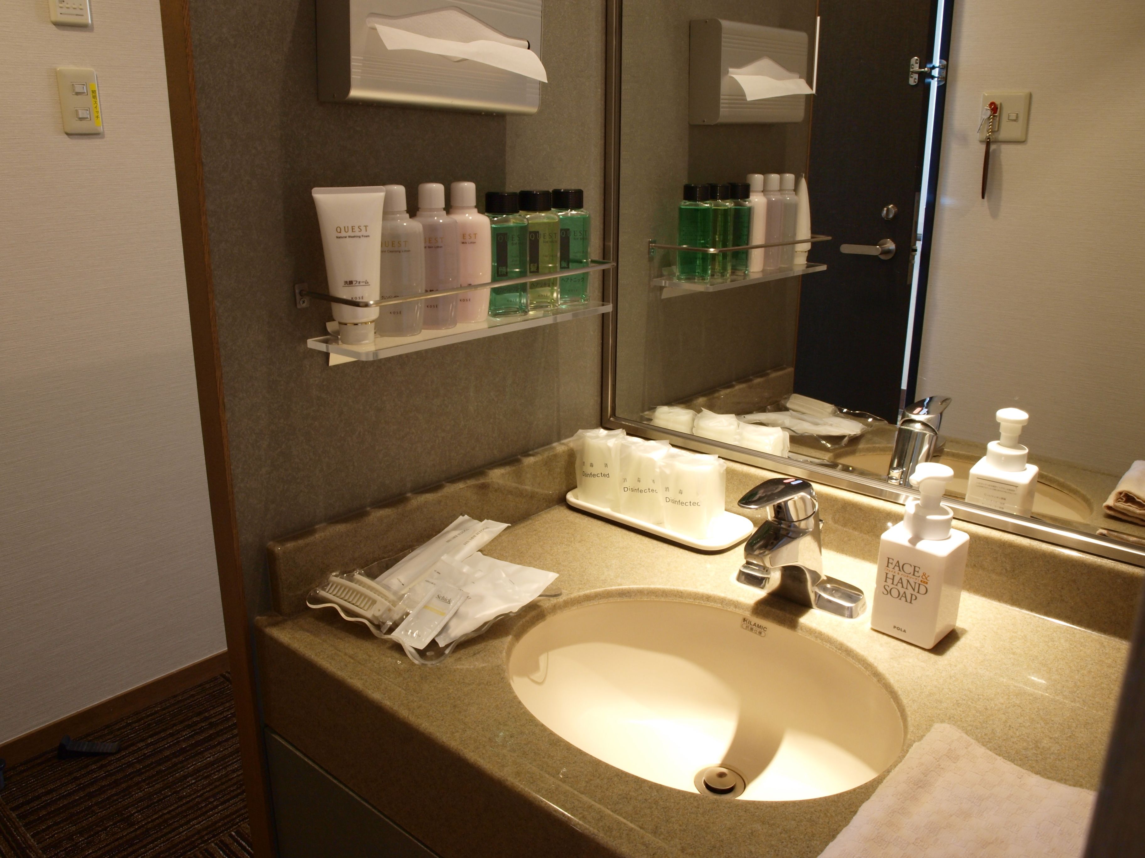 A hotel bathroom with a sink, mirror, and various toiletries on shelves.