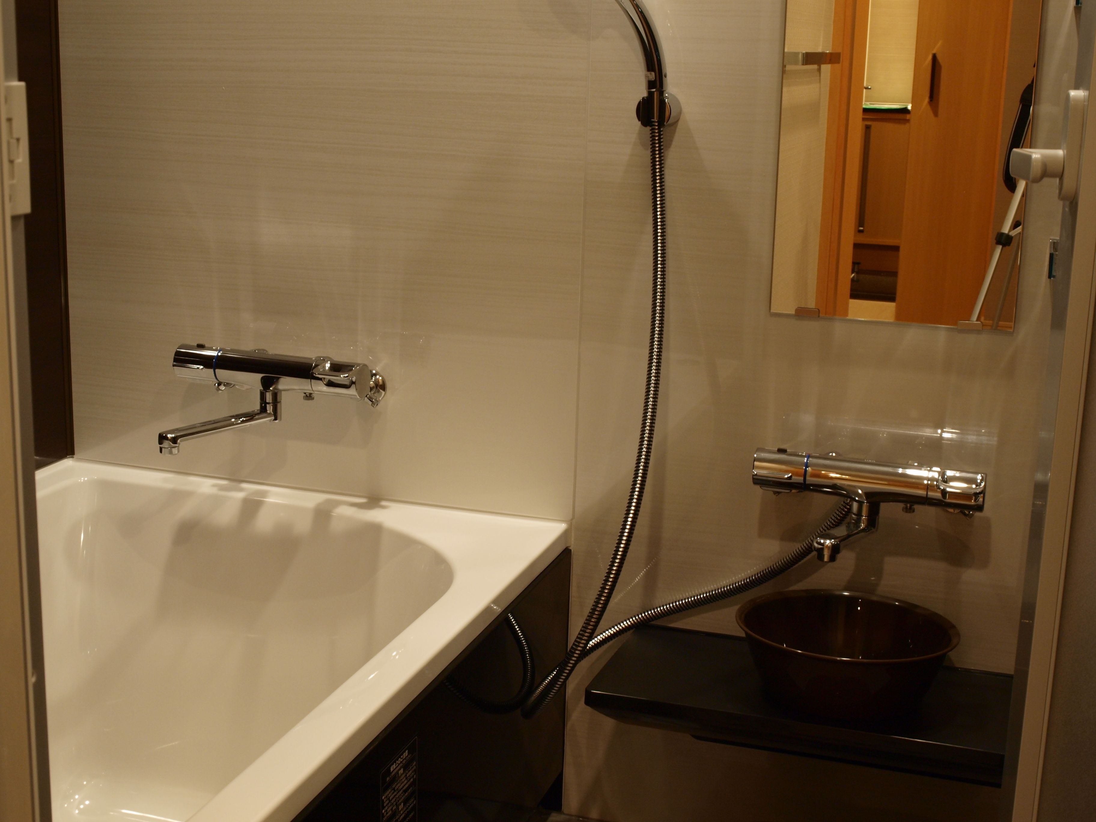 Un bagno con una vasca da bagno bianca, un soffione doccia manuale e un piccolo lavandino con uno specchio sopra.