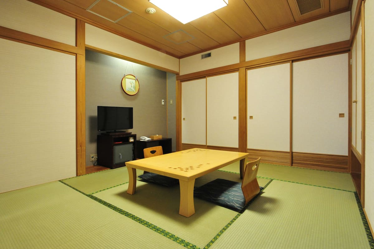 A traditional Japanese room with tatami flooring, a low wooden table, a television, and sliding doors.