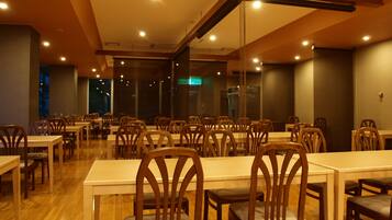 A spacious dining area with wooden tables and chairs, a high ceiling with exposed beams, and a view of the night sky through large windows.