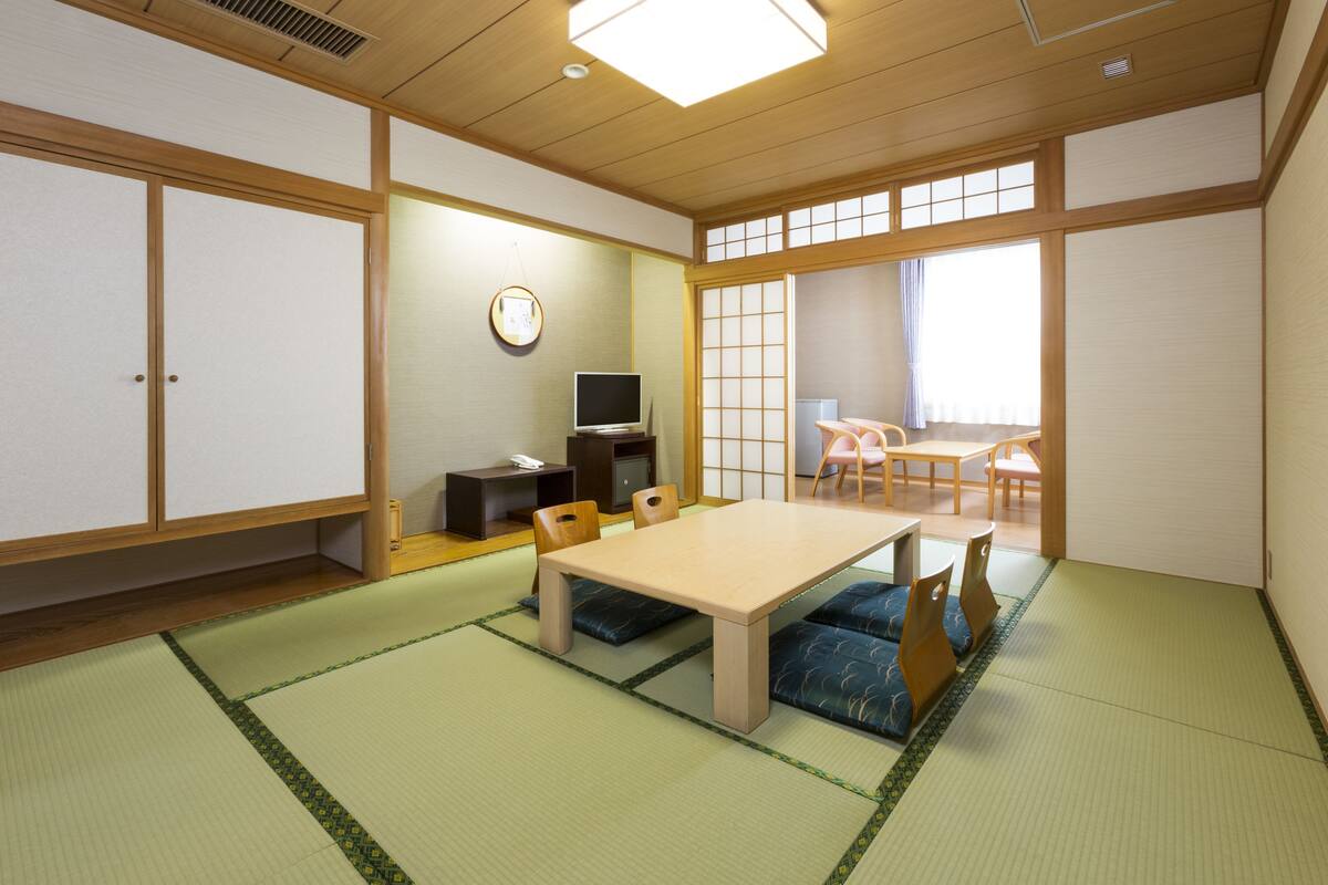 A traditional Japanese room with tatami flooring, a low table with cushions, a television, and sliding doors.