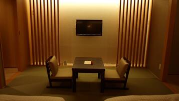 A room with a TV mounted on the wall, a small table with chairs, and a bed with a green mat.