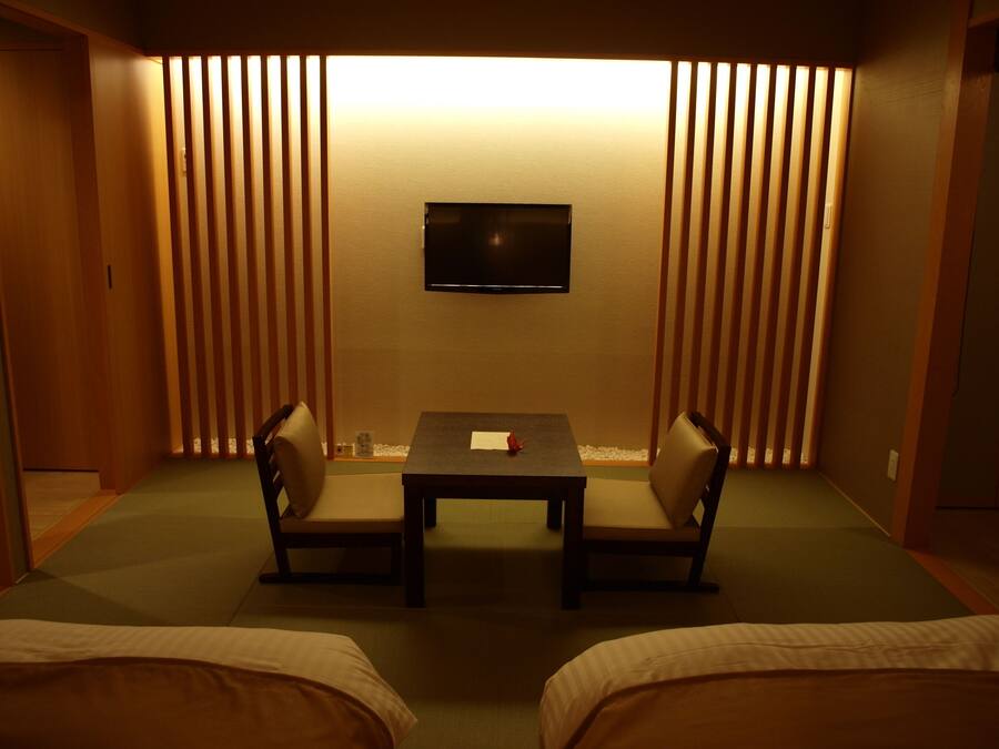 A room with a TV mounted on the wall, a small table with chairs, and a bed with a green mat.