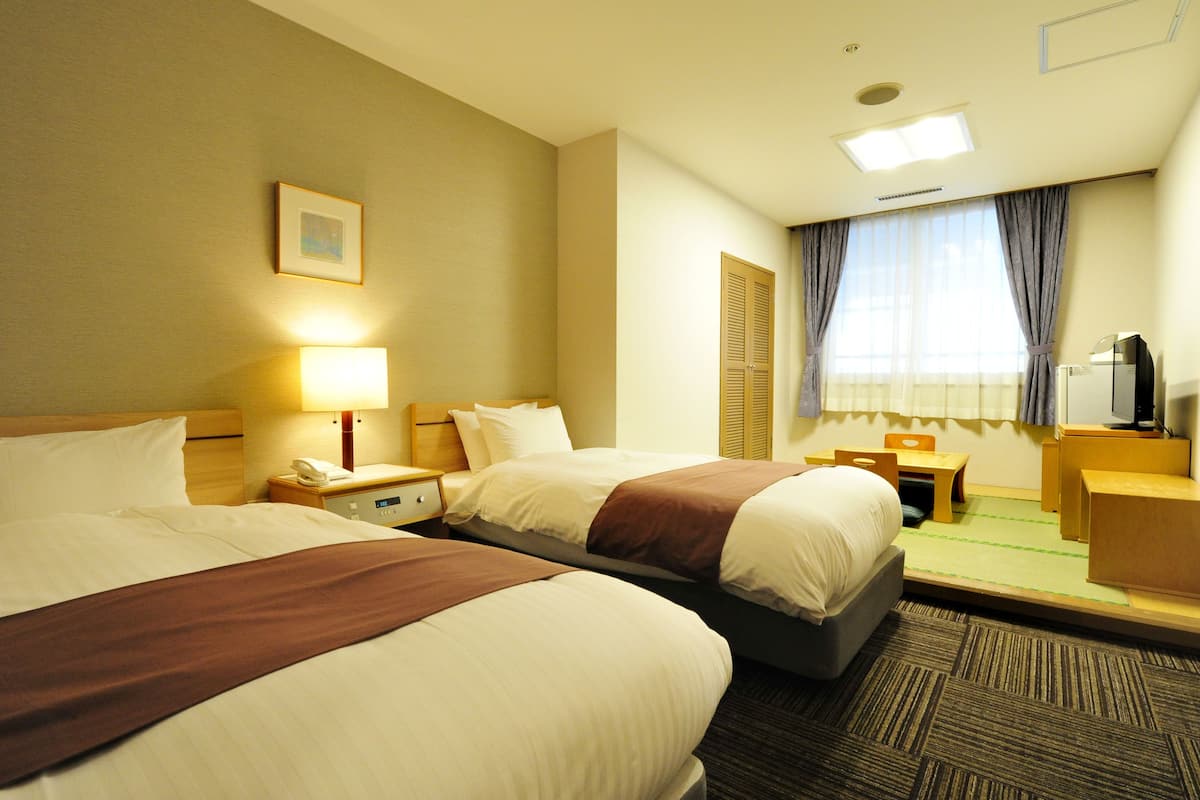 A hotel room with two beds, a desk, a chair, a TV, and a window with curtains.