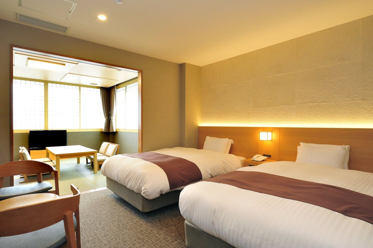A hotel room with two beds, a desk, a chair, and a television.