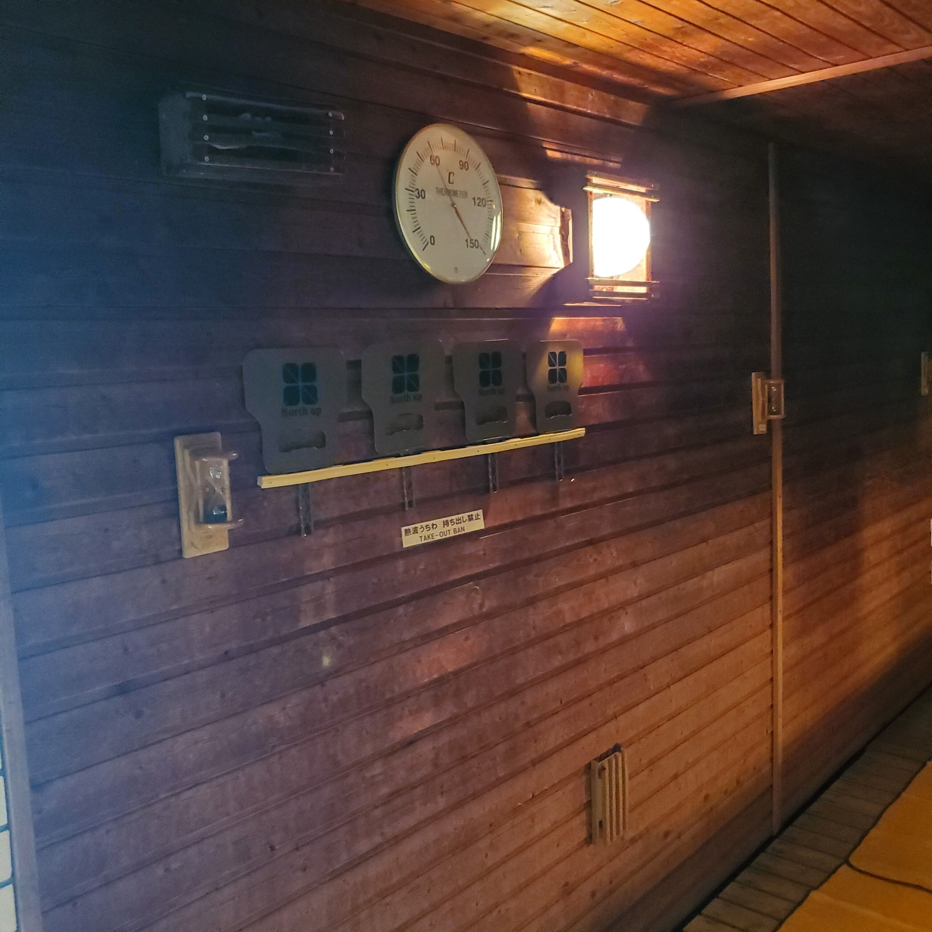 A wooden wall with a thermostat, a clock, and a take-out ban sign.
