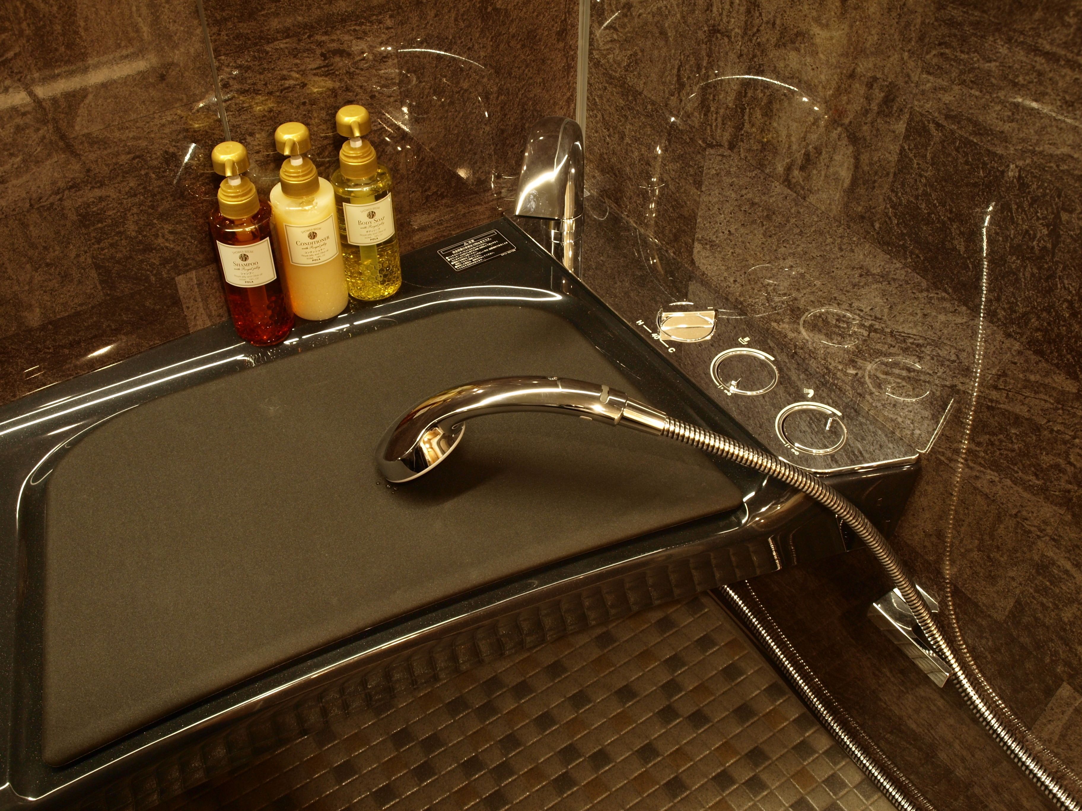 A modern bathroom with a black vanity, a handheld showerhead, and three bottles of toiletries.