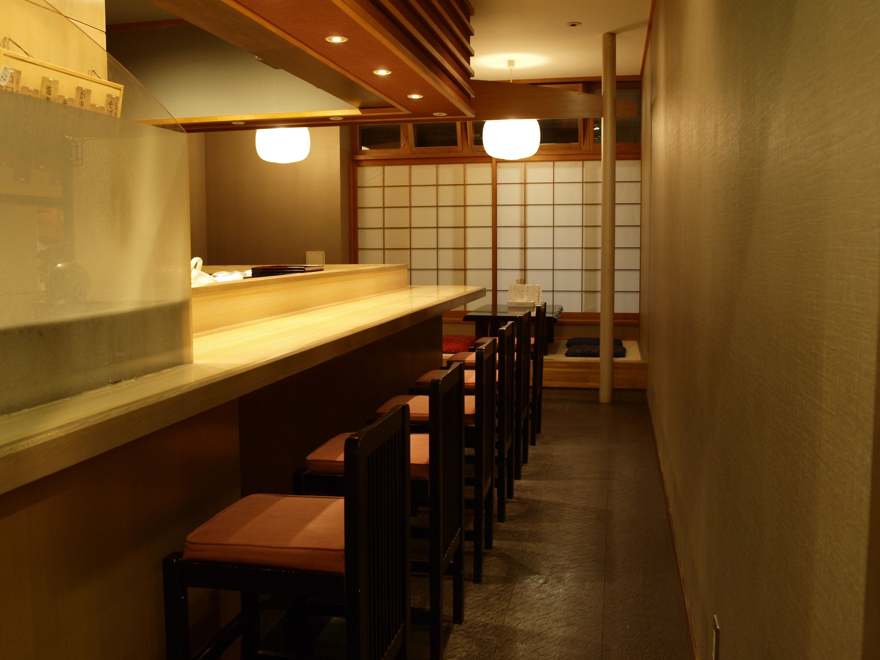 A narrow hallway with wooden benches and chairs, a counter with a menu, and a traditional Japanese sliding door in the background.