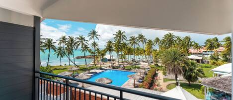 A balcony with a view of a swimming pool, palm trees, and a resort area.
