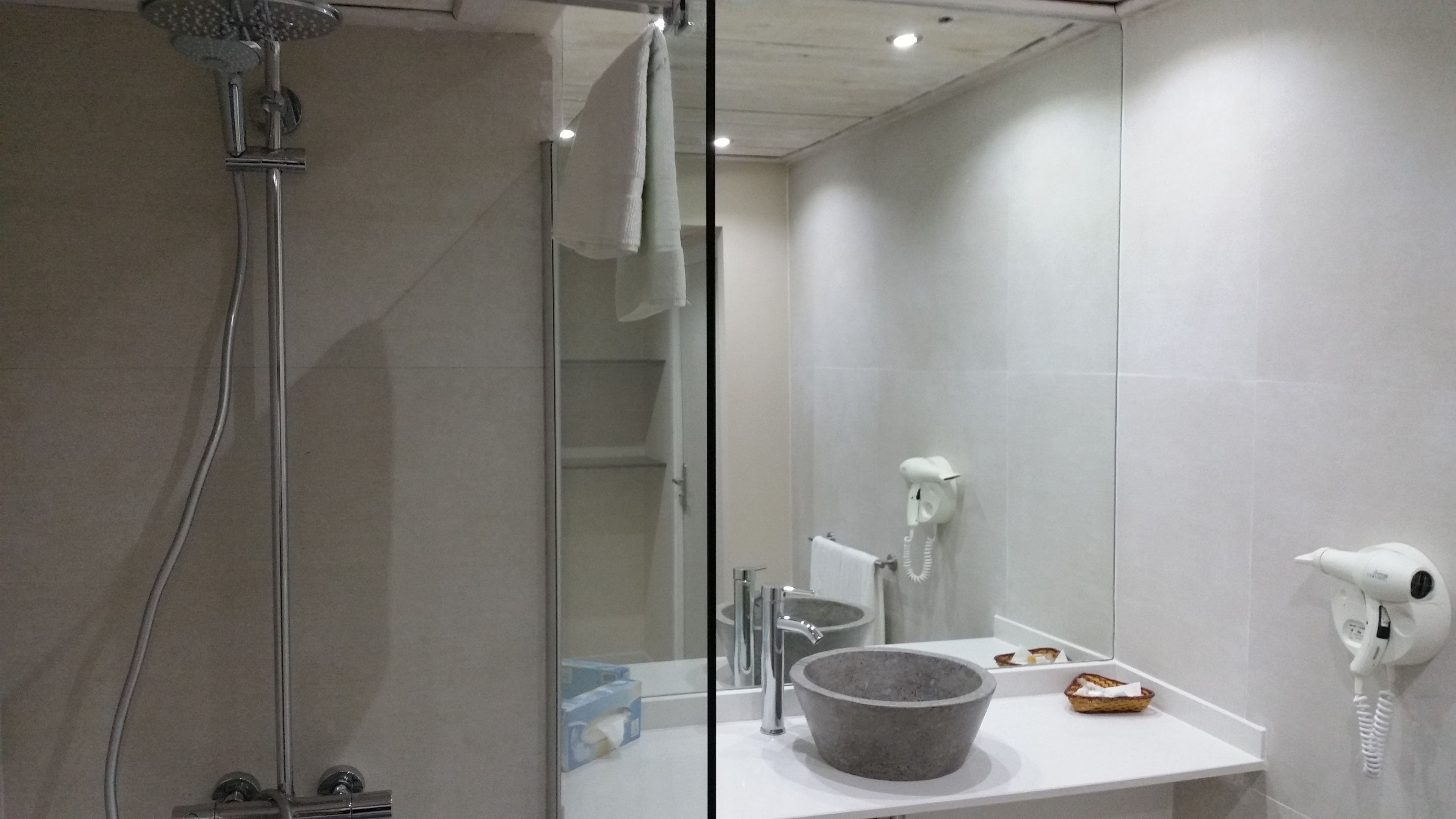 A modern bathroom with a glass shower enclosure, a white sink with a stone basin, and a hairdryer mounted on the wall.