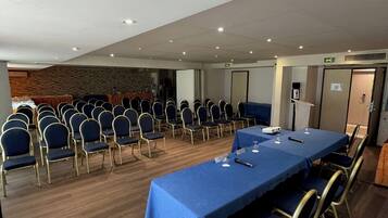 Un salón de conferencias con una larga mesa, filas de sillas y suelo de madera.