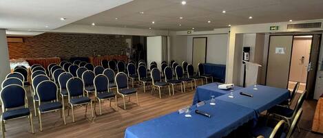 A conference room with a long table, rows of chairs, and a wooden floor.