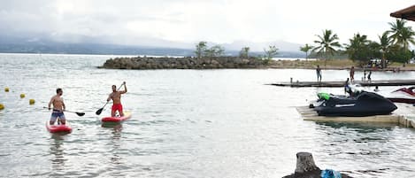 A calm body of water with paddleboards, a jet ski, and a dock with people.