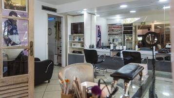 A salon interior with multiple chairs, a mirror, shelves with products, and a television.
