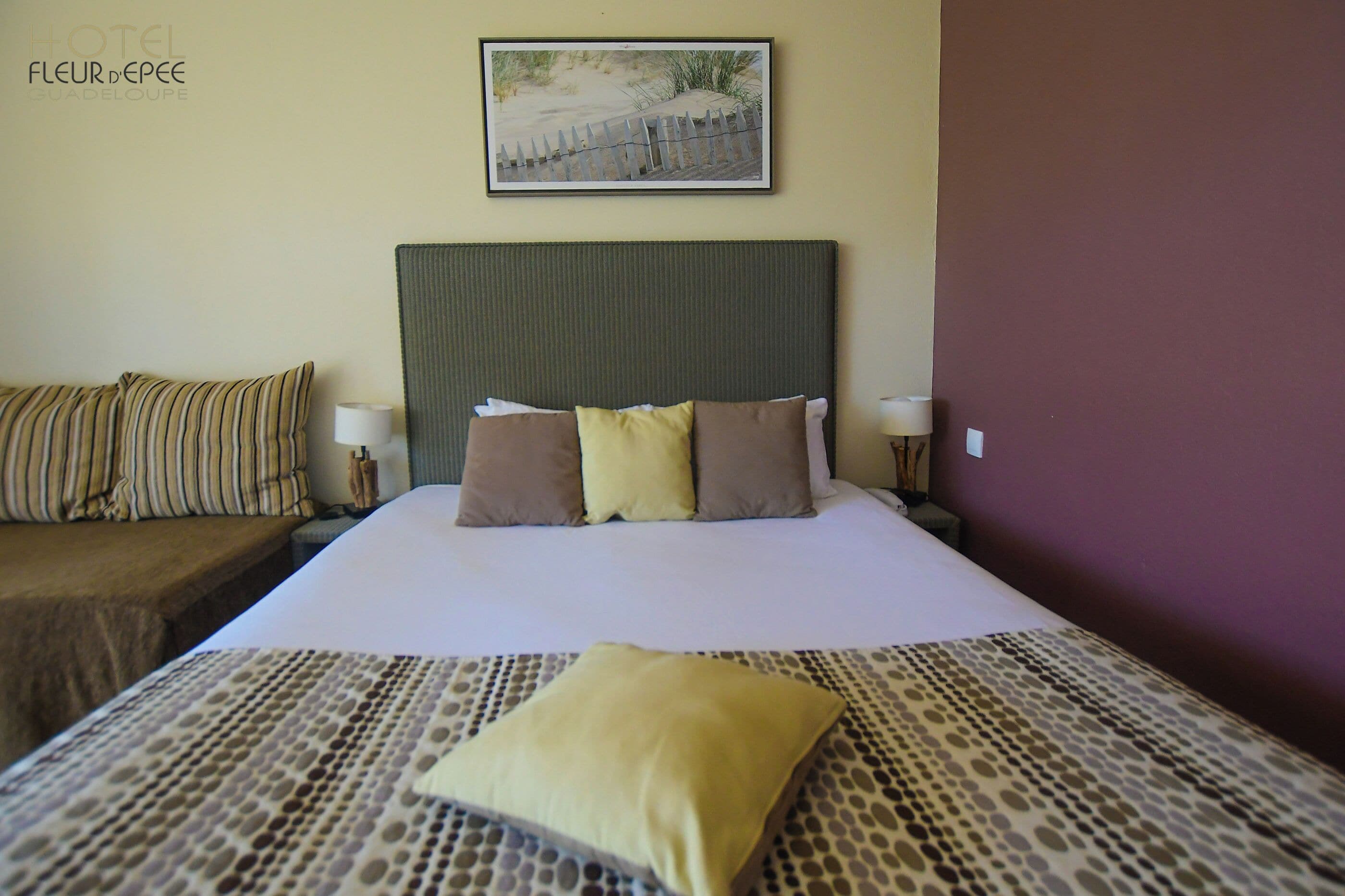 Habitación de hotel con cama, cabecera, mesita de noche, lámpara y un cuadro colgado en la pared.