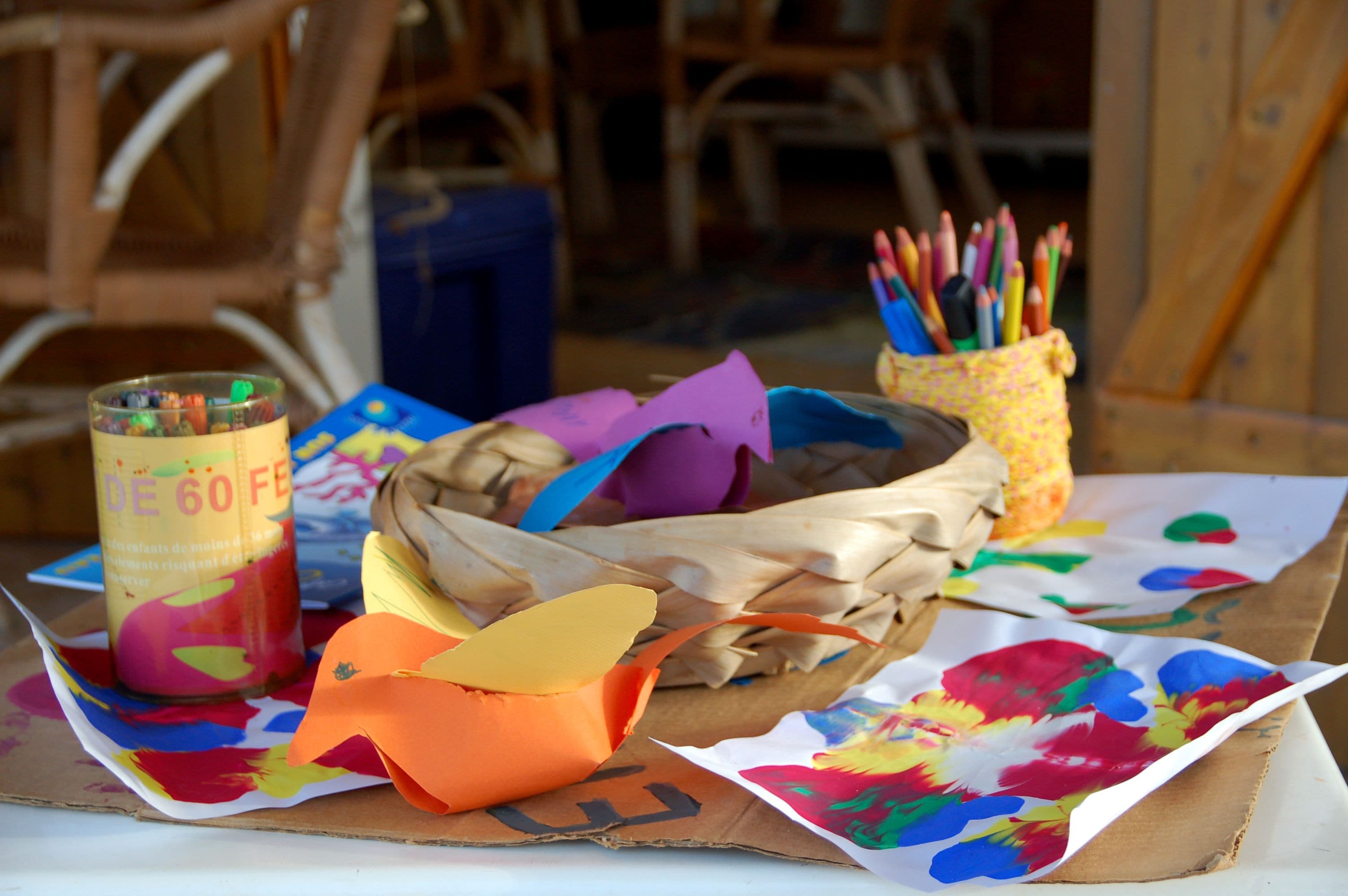 Une table avec un panier, une boîte de peinture multicolore et un pot de crayons.