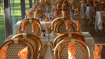 Een terras met eettafels gedekt voor meerdere gasten, met rieten stoelen en witte tafelkleden.