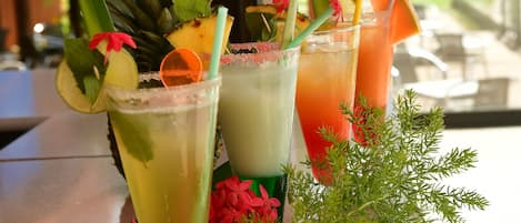Three tropical cocktails on a table with a view of palm trees and a building in the background.