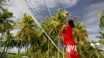 A person playing volleyball on a beach with palm trees and a clear sky in the background.
