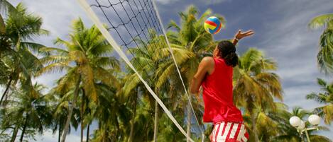 A person playing volleyball on a beach with palm trees and a clear sky in the background.