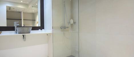 Une salle de bain moderne avec une douche à l’italienne en verre, un lavabo blanc avec un receveur en pierre et un grand miroir au-dessus du lavabo.