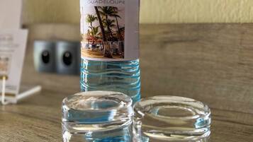 Una botella de agua Hotel Fleur de Epee Guadeloupe, dos vasos y una servilleta sobre una mesa de madera.