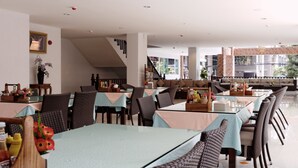 A modern restaurant with long tables and wicker chairs, a staircase, and large windows offering a view of the city. - Pattaya Blue Sky (Pattaya)