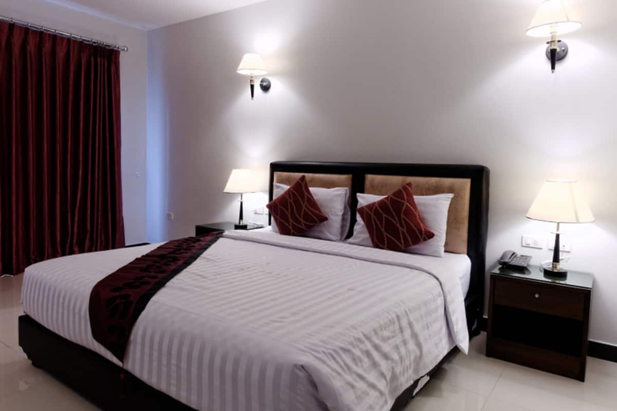 A hotel room with a large bed, two bedside tables with lamps, a red curtain, and a wall-mounted light fixture.