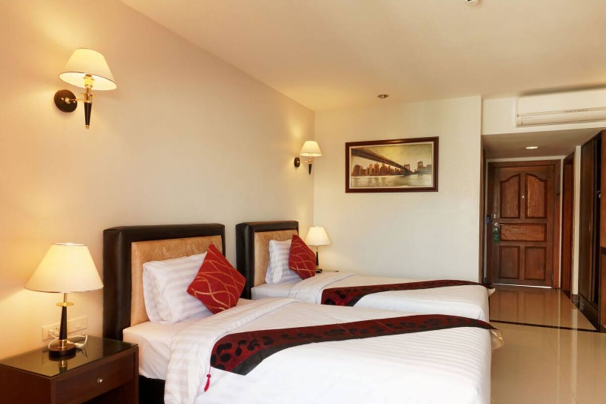 A hotel room with two beds, nightstands, wall-mounted lamps, a framed picture, and a door.