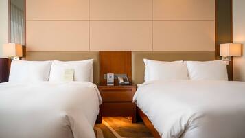 A hotel room with two beds, a wooden headboard, bedside lamps, a nightstand with a phone and a menu, and a carpeted floor.