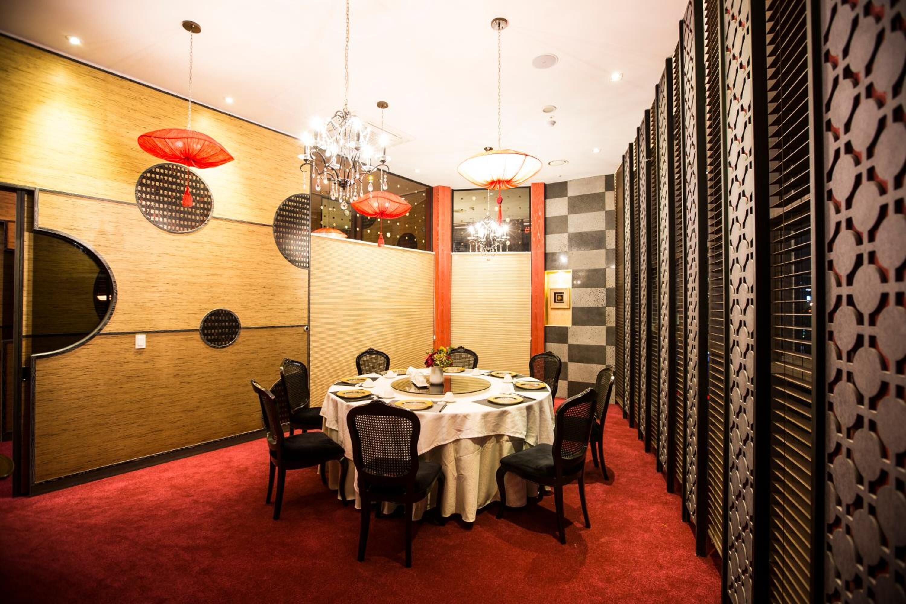 A dining area with a round table set for six, surrounded by chairs, with a red carpet on the floor.