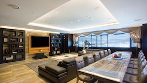 A modern living room with a large flat-screen TV, a dining table with leather seating, and a bookshelf. - Isquare Hotel (Gimhae)