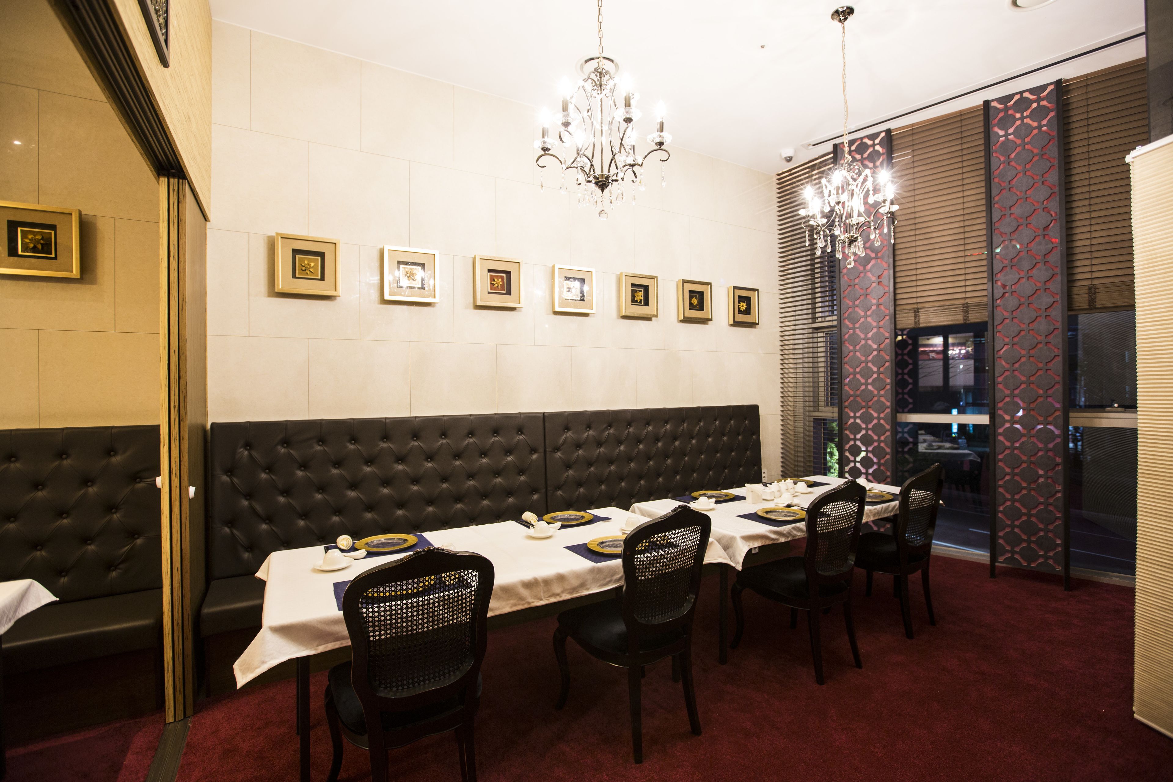 A dining area with a long table set for four, surrounded by black upholstered booths and chairs.
