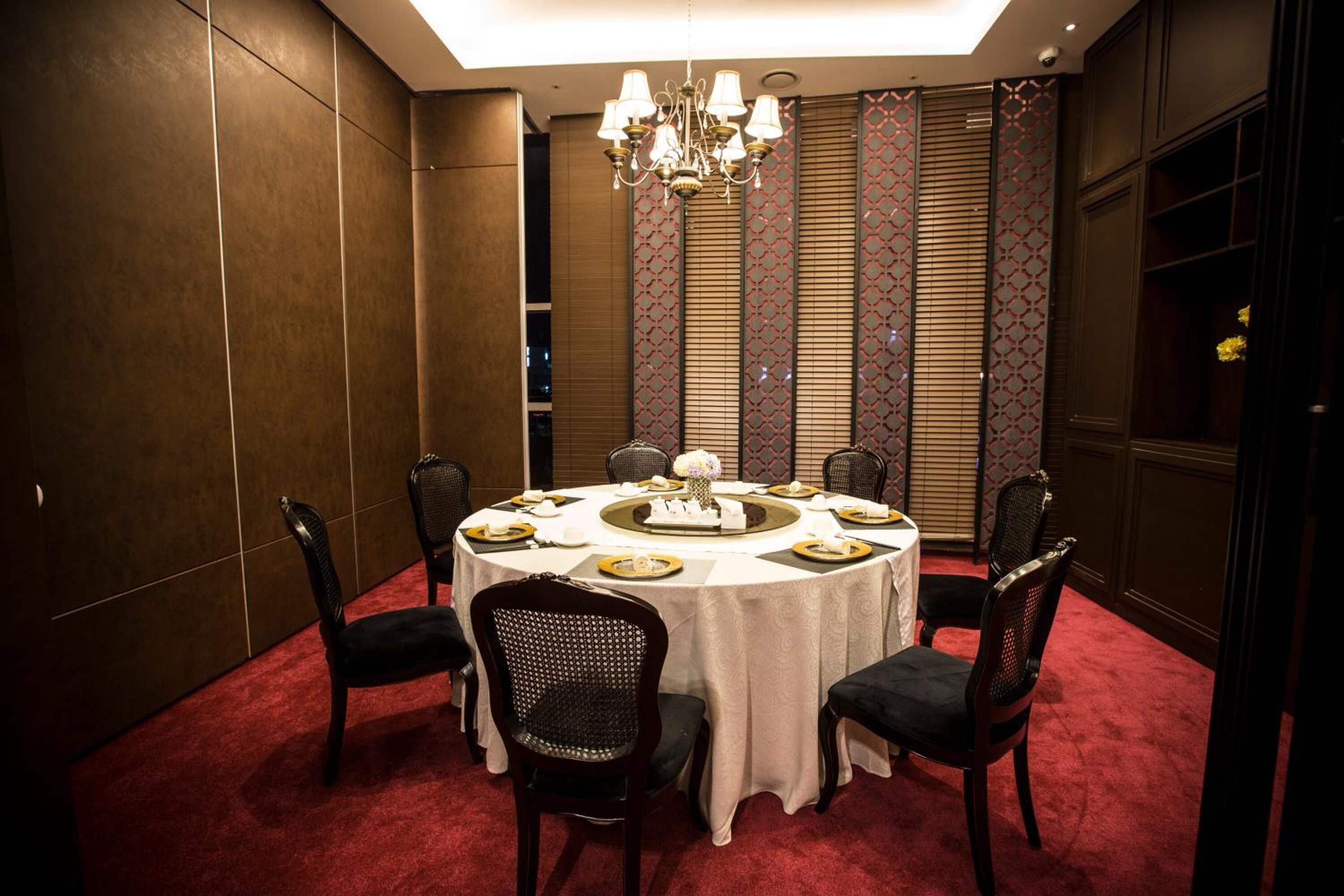 A dining room with a round table set for six, surrounded by dark upholstered chairs.