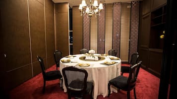 A dining room with a round table set for six, surrounded by dark upholstered chairs.