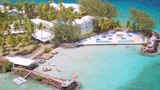 An aerial view of a beach resort with a swimming area, palm trees, and a dock with boats. - Résidence La Marina (Trois-Ilets)