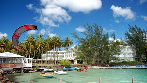 A beachside hotel with a parasail, palm trees, and a clear blue sky. - Résidence La Marina (Trois-Ilets)