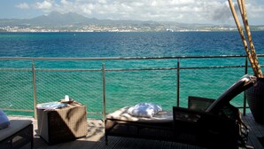 A deck with wicker furniture, a small table, and a view of the sea and distant mountains. - Résidence La Marina (Trois-Ilets)