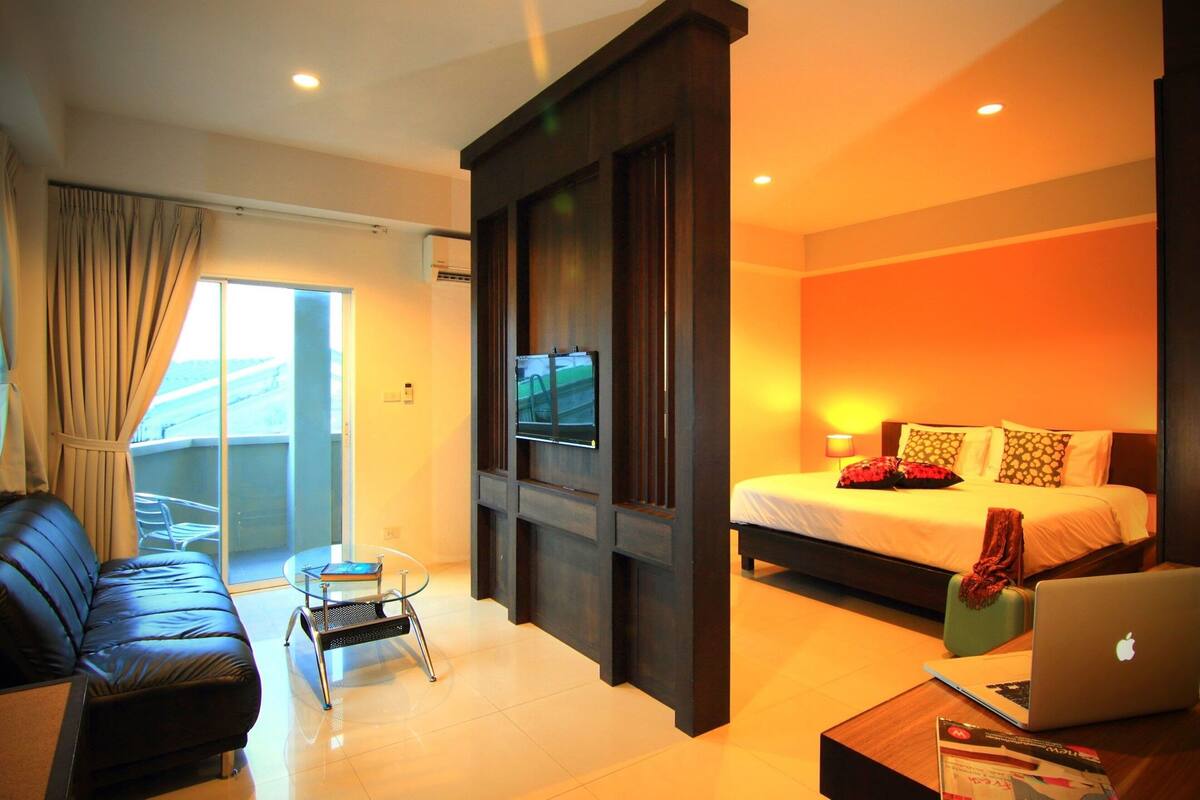 A modern hotel room with a sofa, a small table, a laptop, a bed, and a TV.