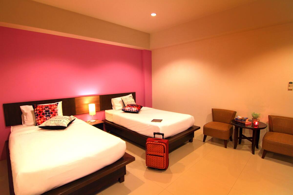 A hotel room with two beds, a small table with a lamp, and a chair.
